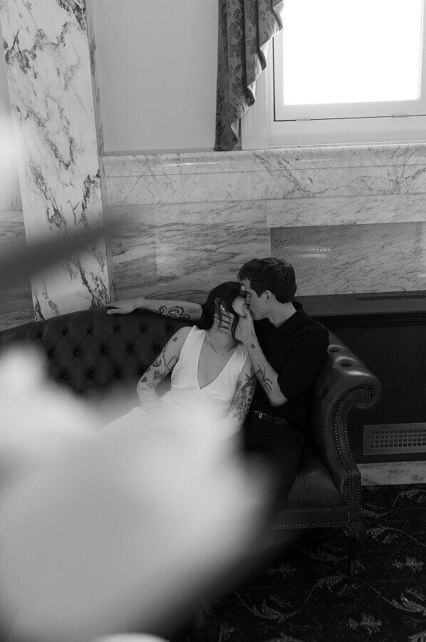 A black and white photo of a man kissing his soon-to-be wife. They're both sitting on a leather couch.
