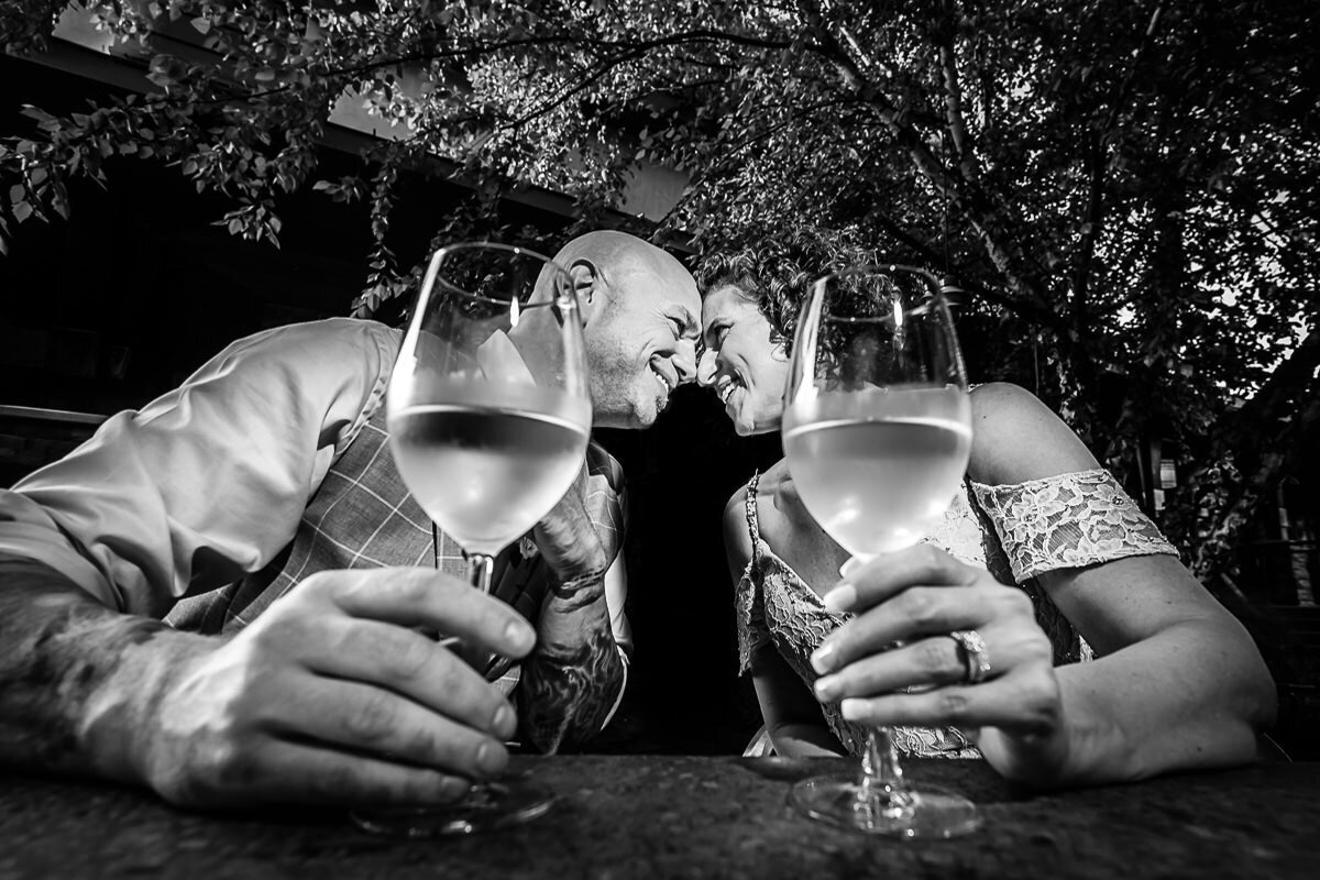 A groom and bride touch foreheads over their glasses of wine