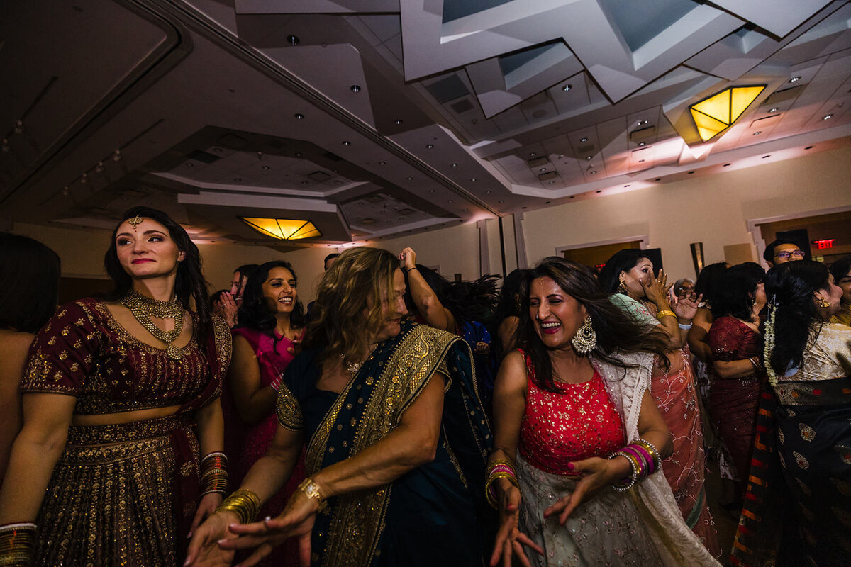 Women in colorful Indian attire dance joyfully at a wedding reception