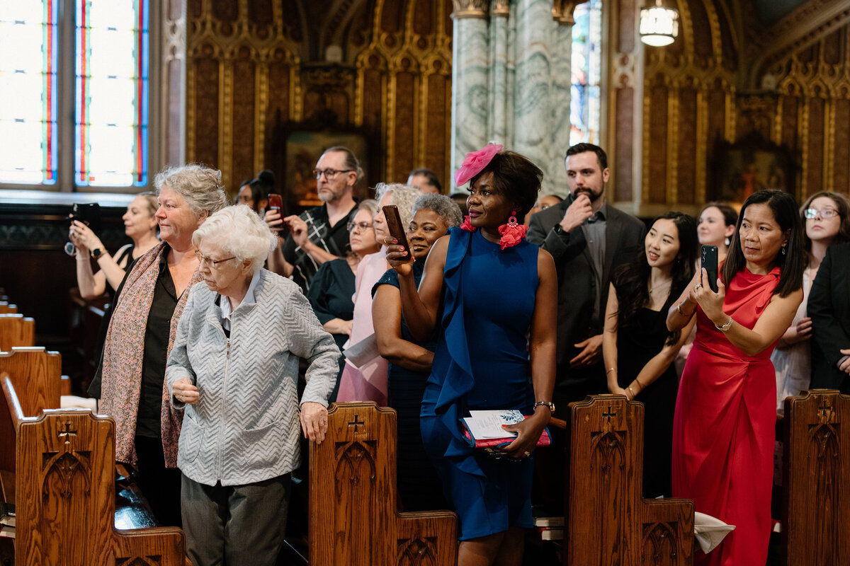 All the wedding guests standing and watching as the bride walks down the aisle and toward the altar