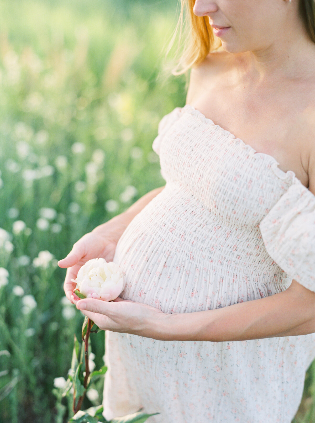 Maternity Devner Photographer Featuring  client standing in field holding flower.