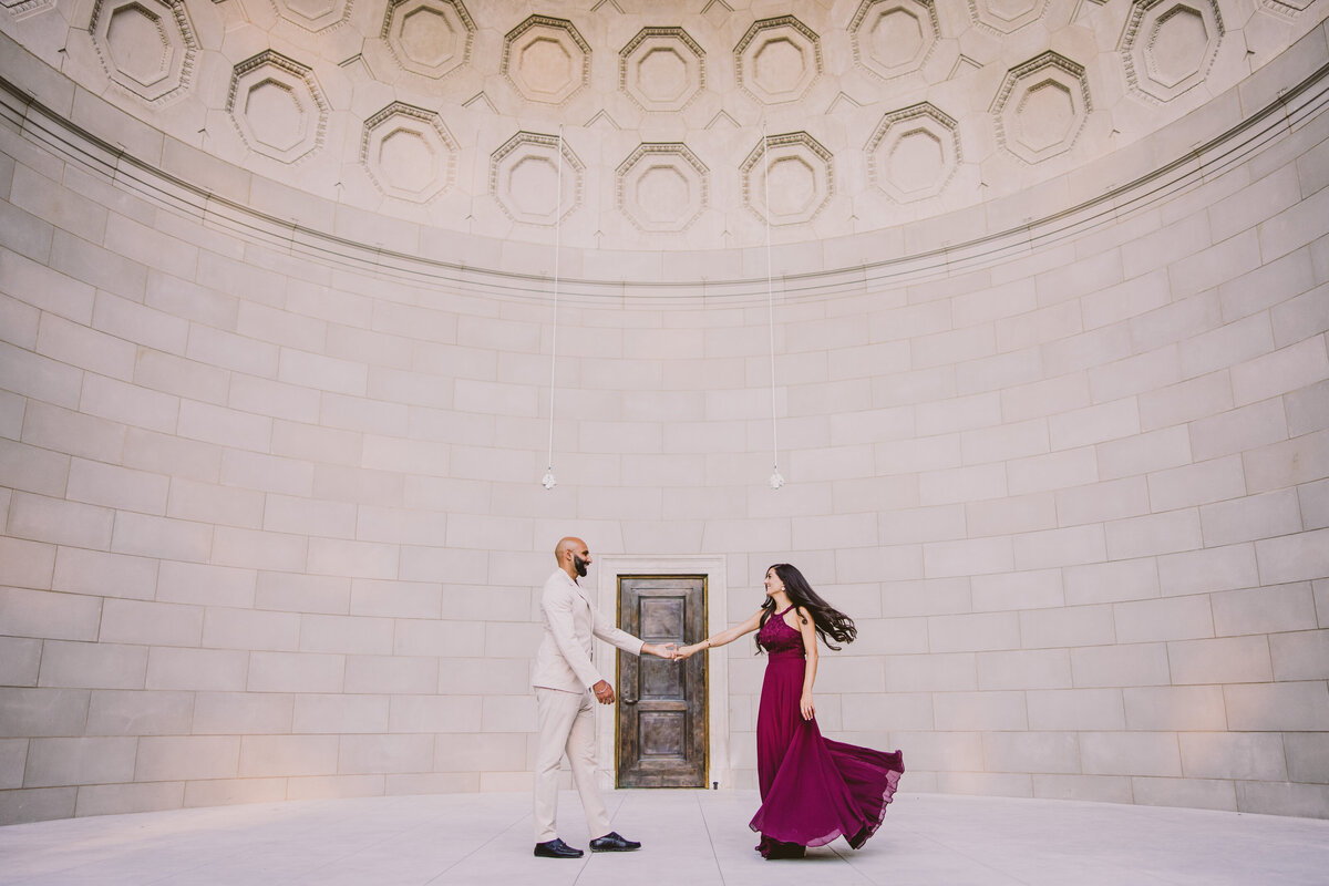 Groom twirling the bride in red formal outfits at central park during their engagement session inside the bandshell at central park