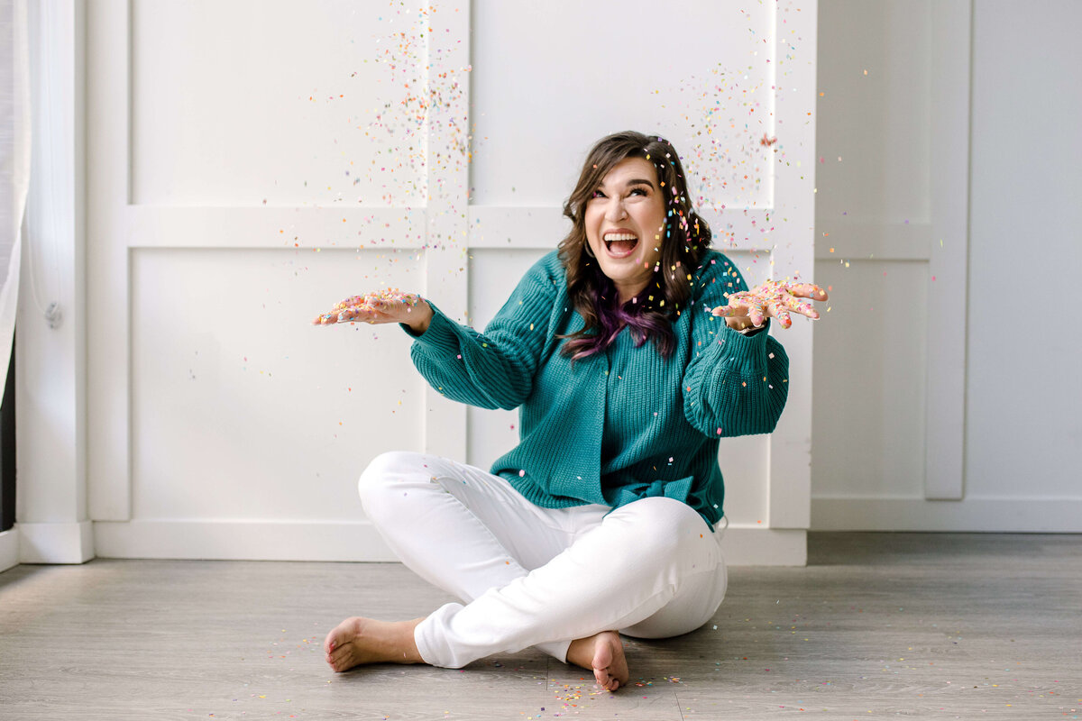 Woman and a T-shirt and white pants sets Kris Kross on the floor of a photo studio and throws confetti in the air and celebration for her personal branding photo shoot