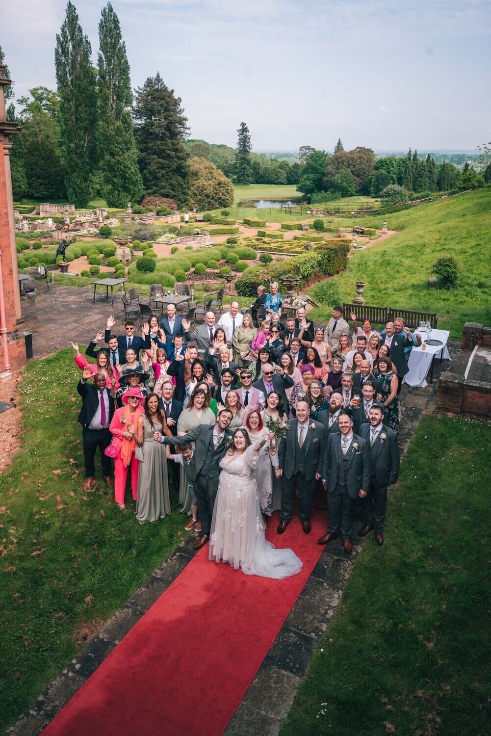 Whole wedding party  outside venue look up at camera from a distance