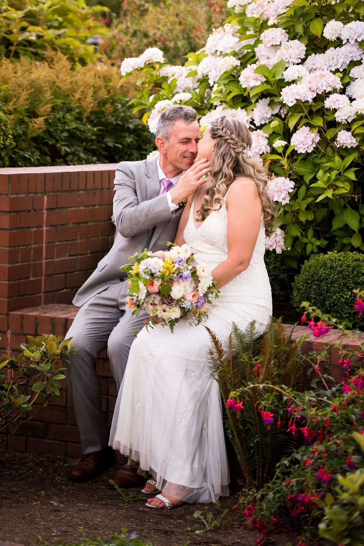 Groom leans in to kiss a bride and she hold her flower bouquet.