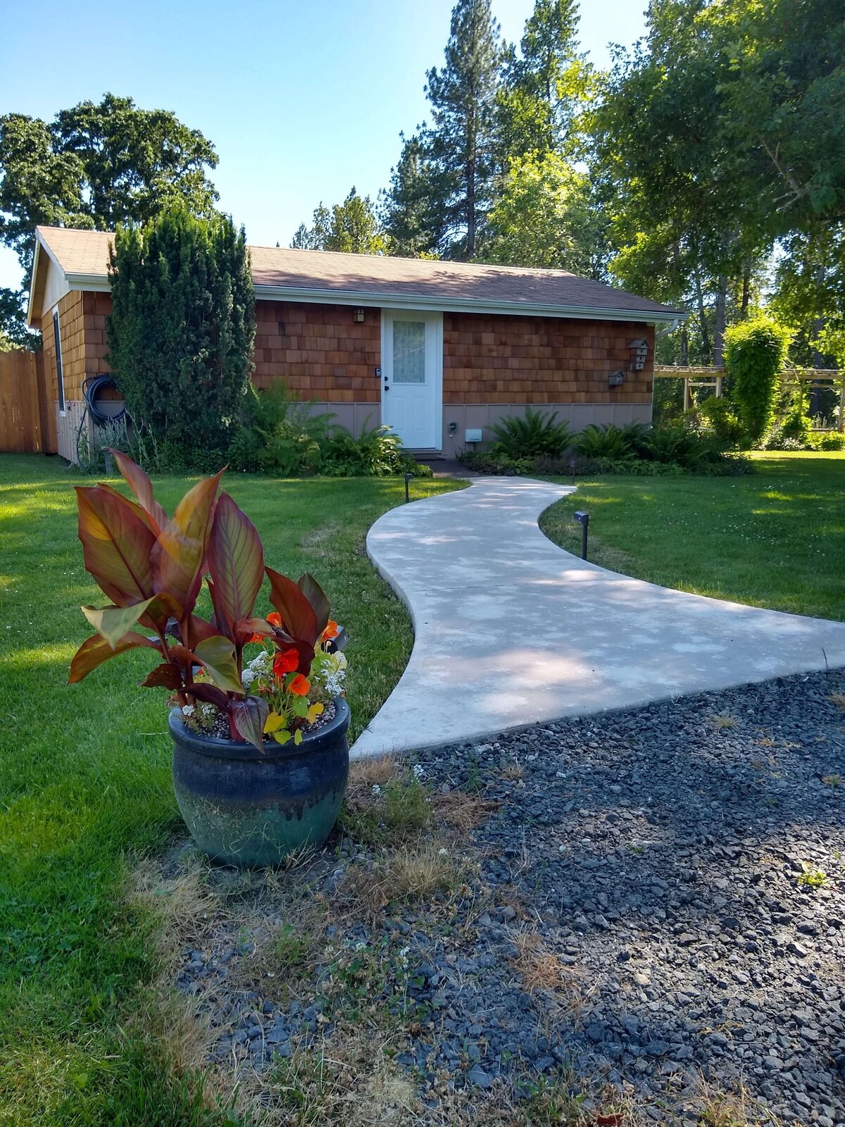 Gravel parking meets paved walkway leading to cottage with green grass on sides.