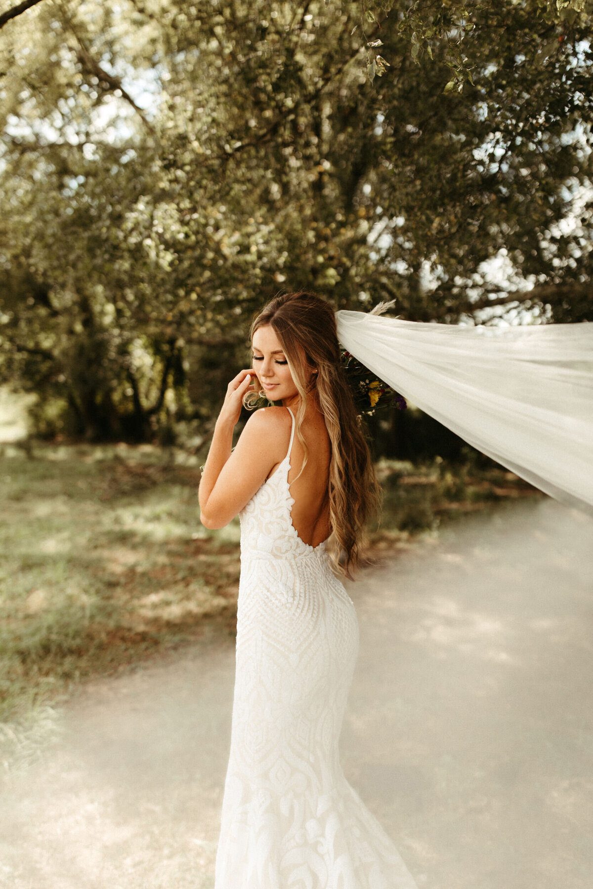 Boho bride in backless wedding dress looking back over her shoulder as the wind blows her cathedral veil