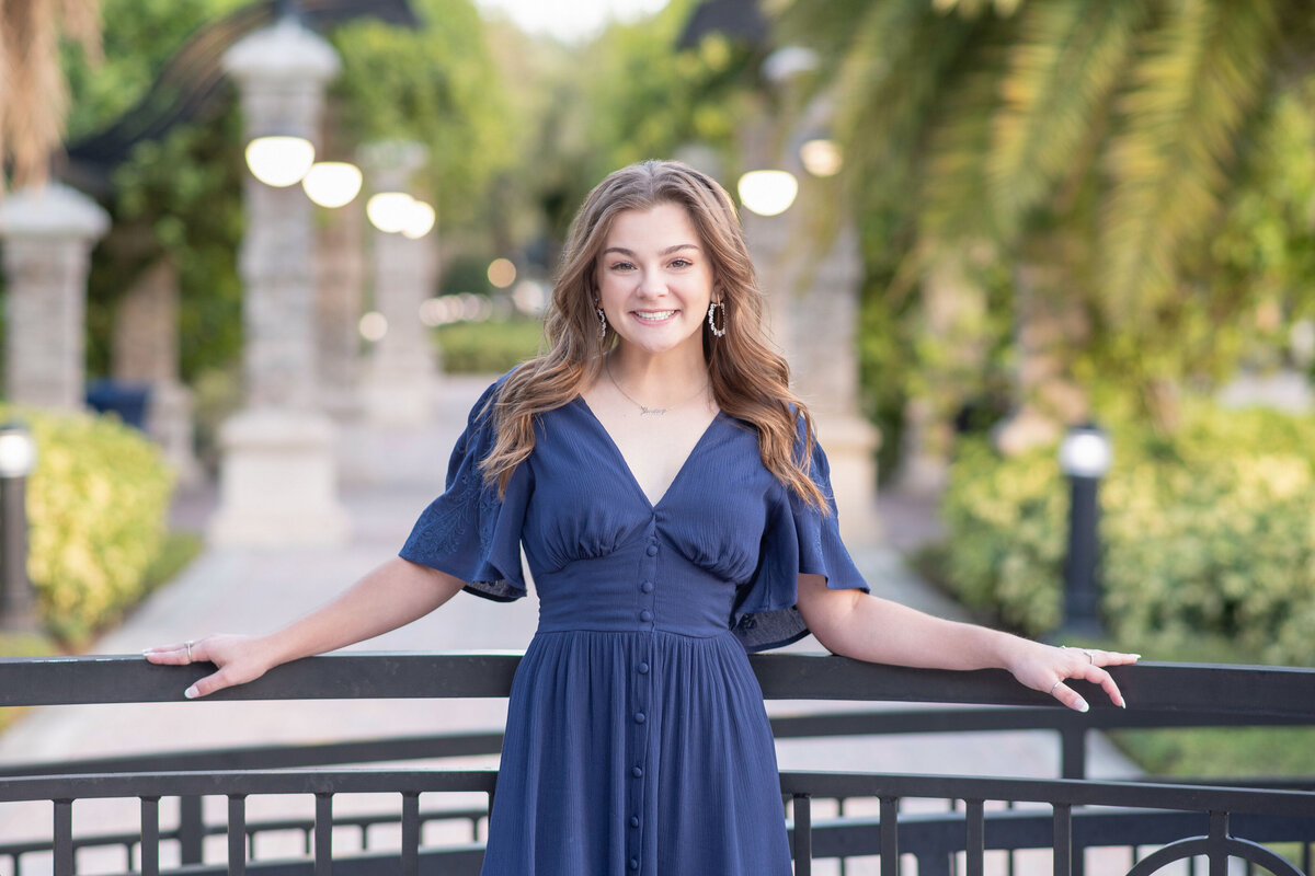 High school senior girl holds railing while smiling at camera.