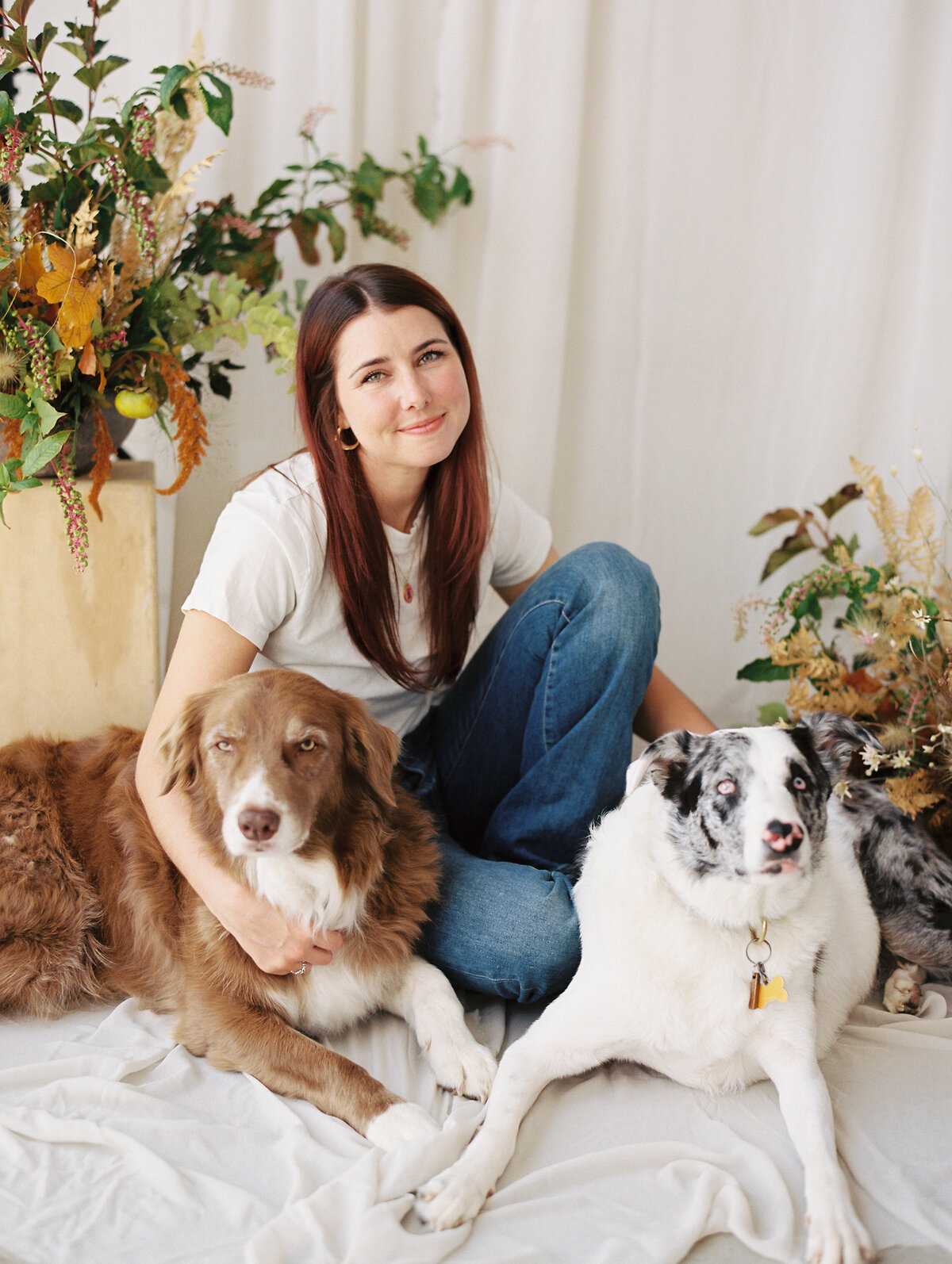 Studio photo of a woman with her two dogs with florals and greenery in the background