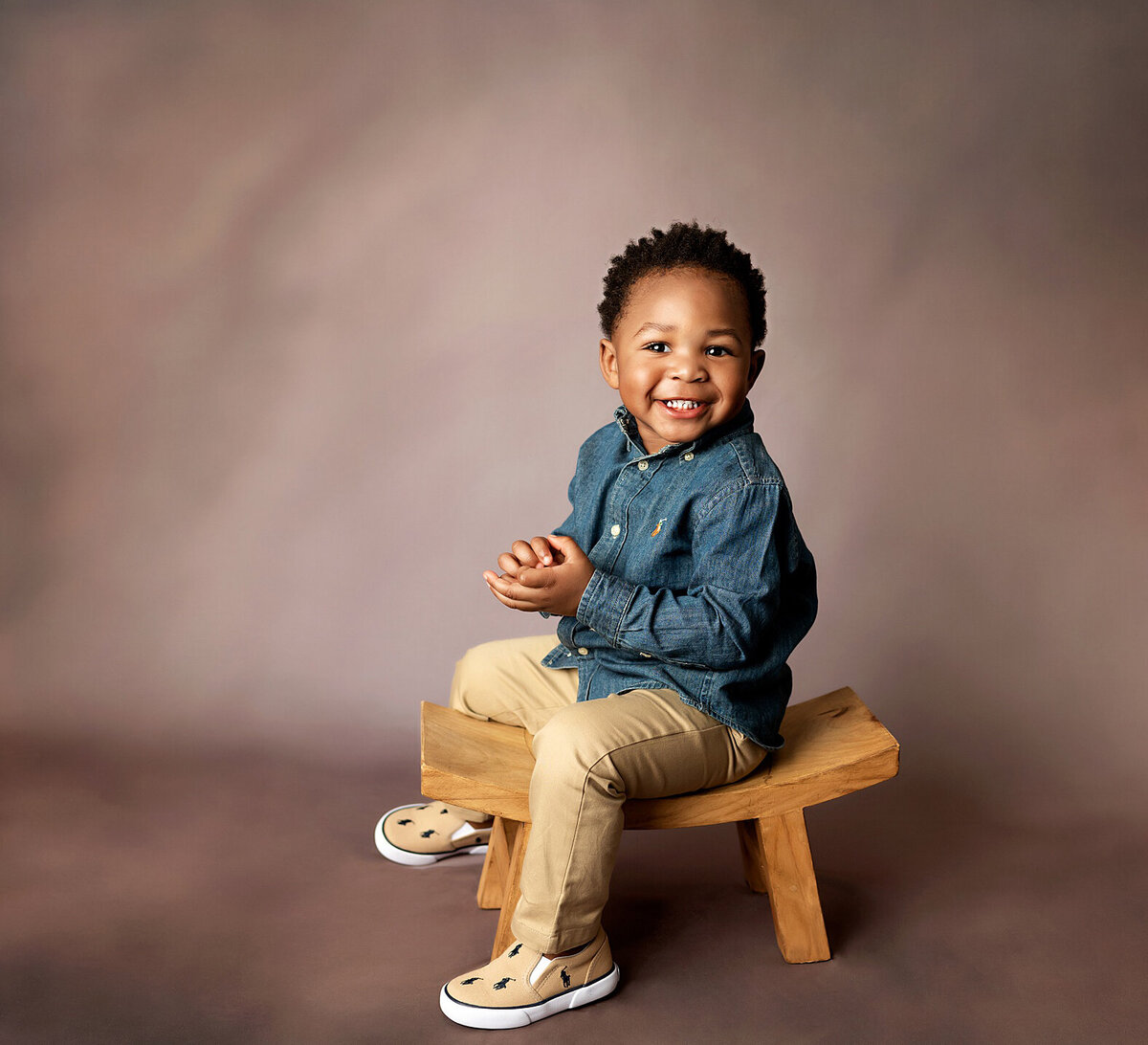 A young boy with a bright smile posing on small bench.