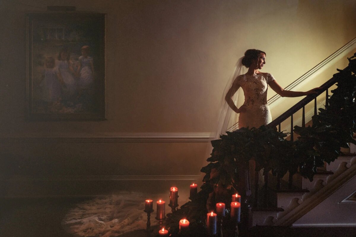 A bride standing on a staircase decorated with florals and candles