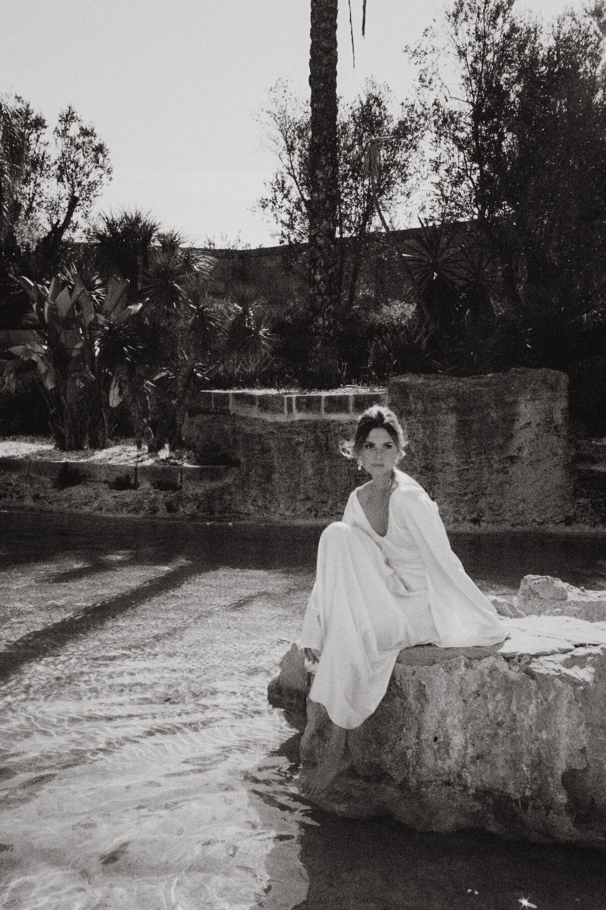 Bride in elegant white dress sitting near rustic pool by Wedding Photographer France