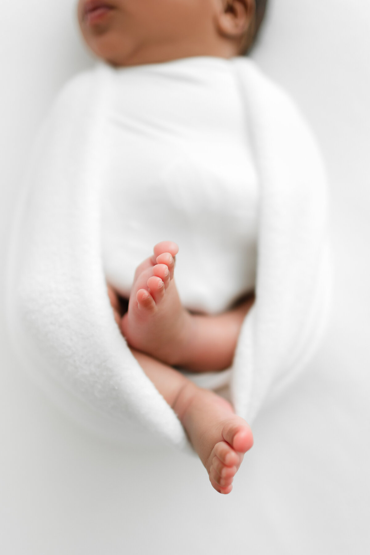 A closeup Virginia Newborn Photographer photo of a baby girl's feet swaddled in a white blanket