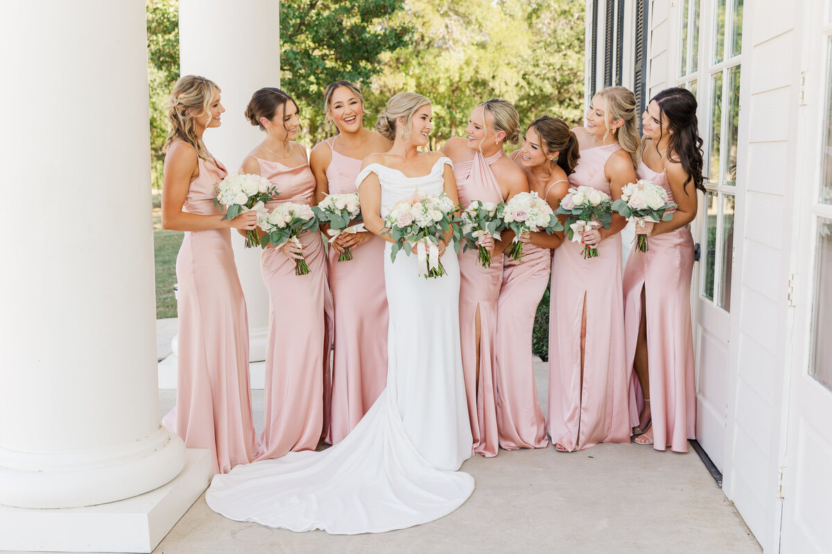The bride and her bridesmaids share a joyful moment on a classic white porch, a delightful scene of Southern charm in Denton, Texas.