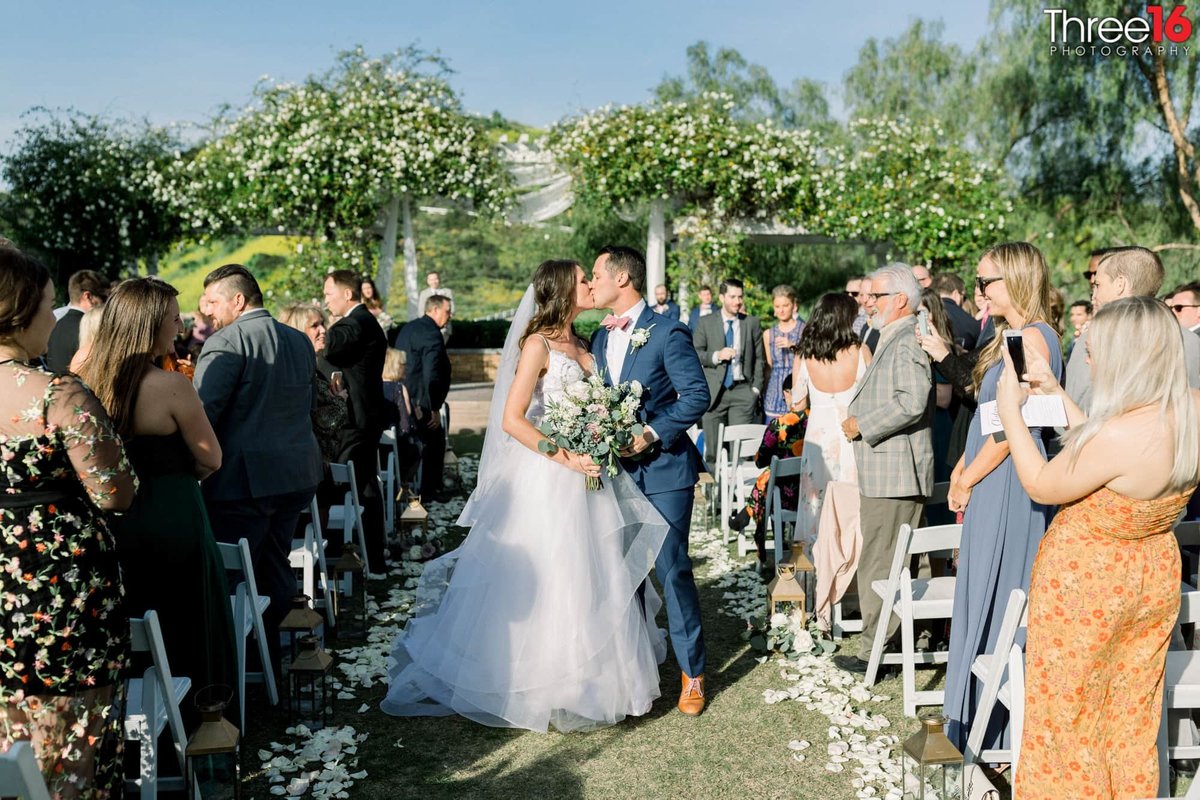 Newly married couple stop along the aisle to share a kiss with one another