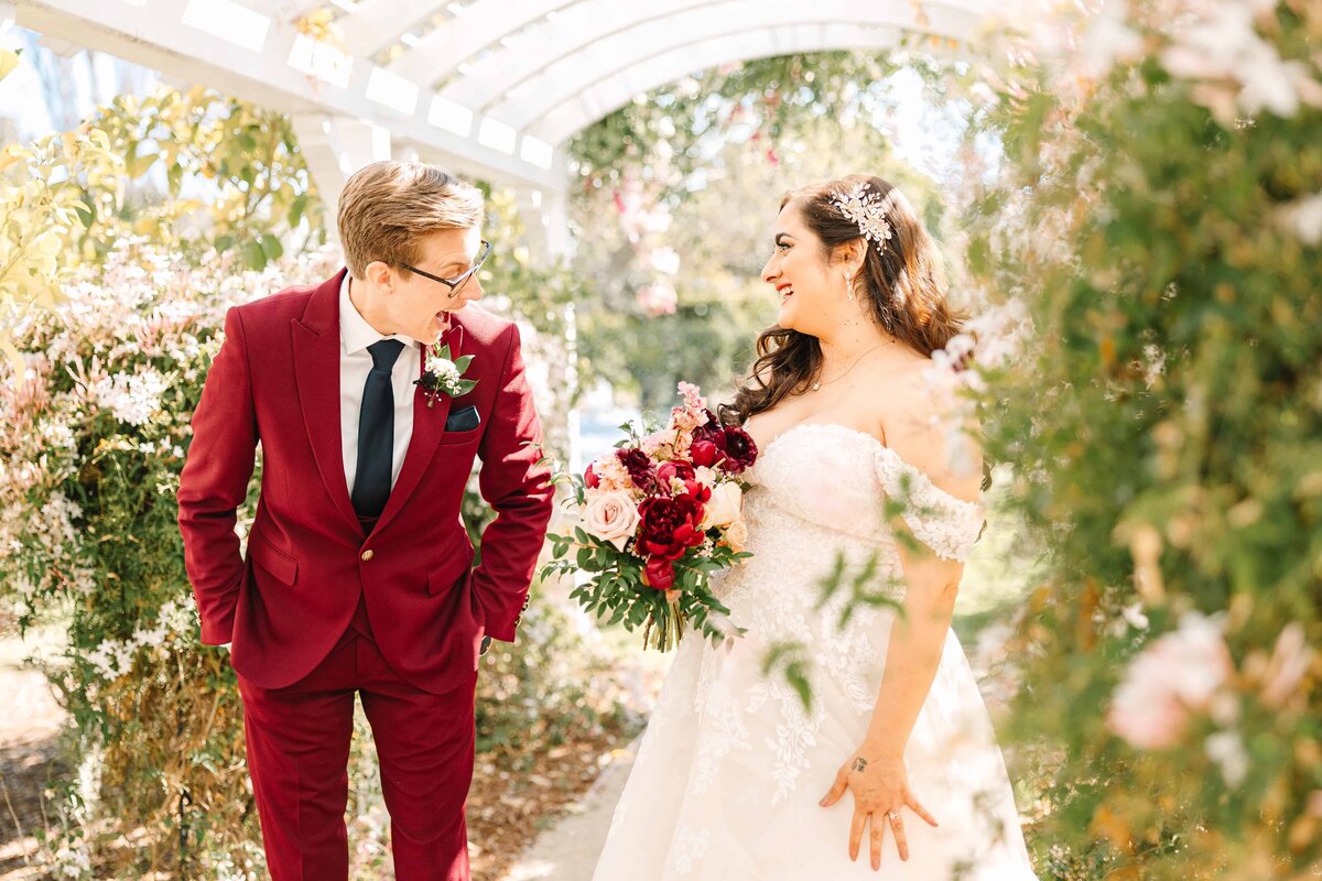 first-look between two brides at madonna inn with the first bride wearing a sharp maroon suit reacting to her beautiful bride in her full ball gown