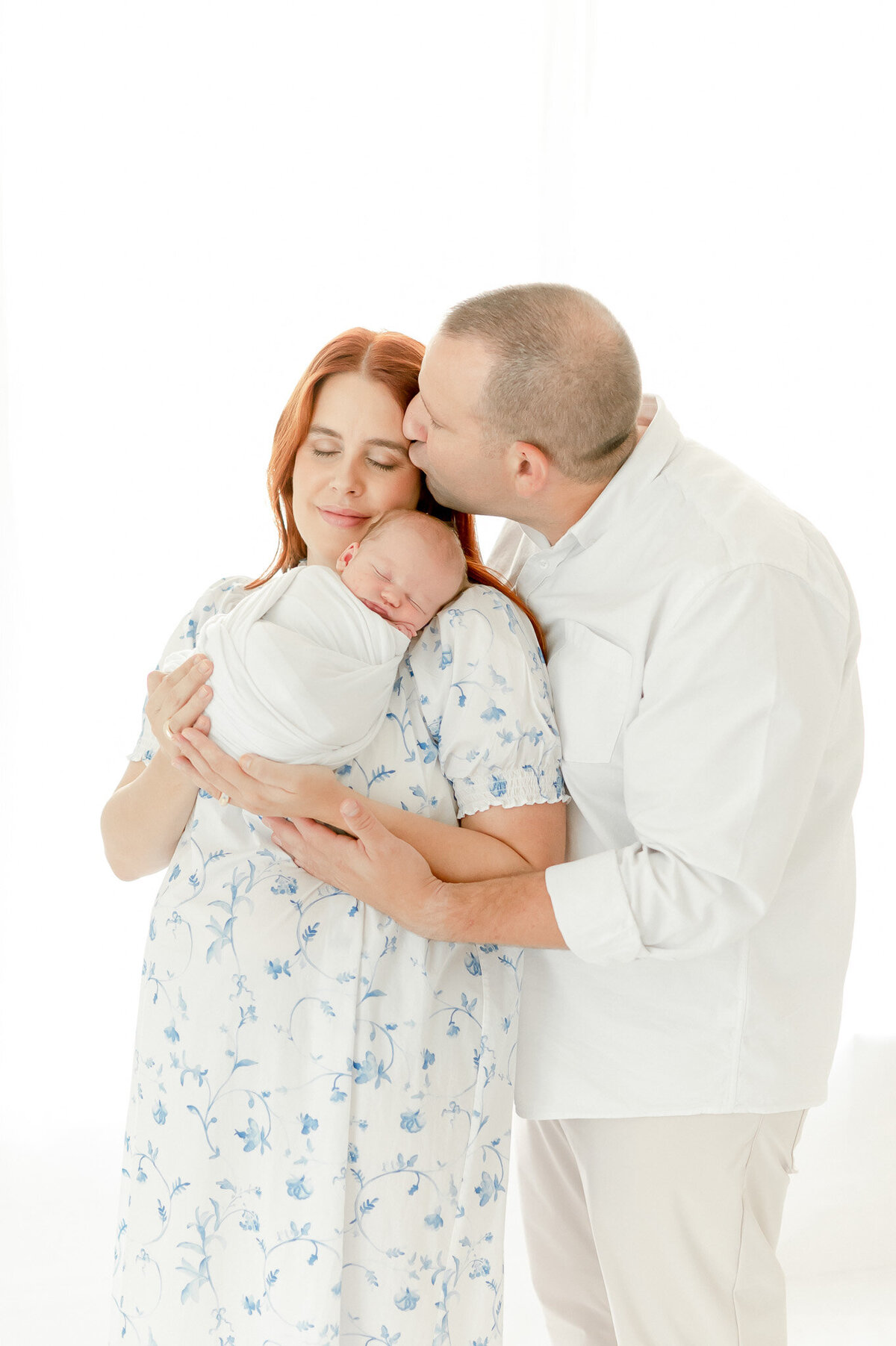 man kisses his wife holding a newborn In Kristie Lloyd’s Nashville newborn photographer studio