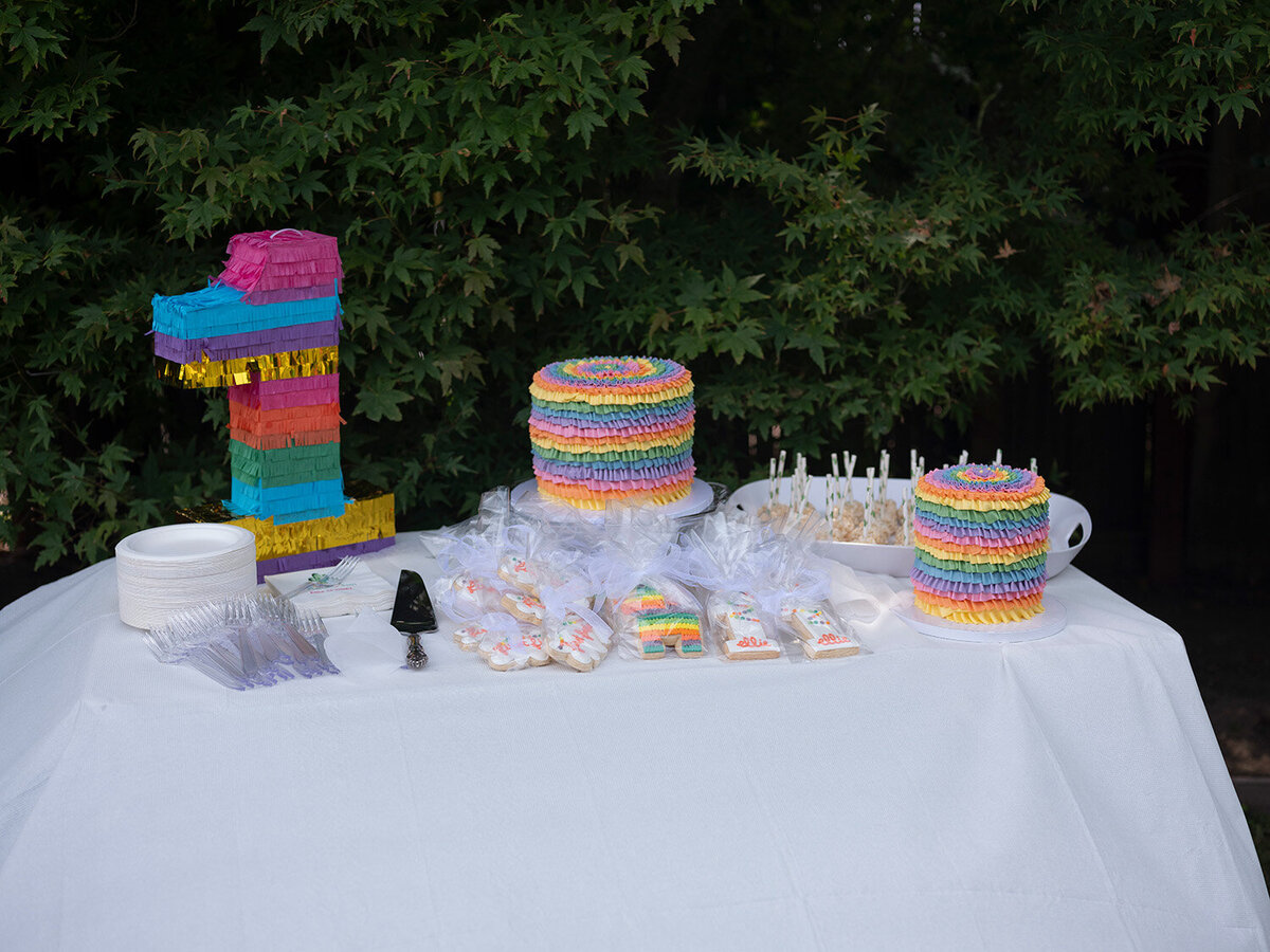 Table with a variety of birthday cakes and desserts set up for a first birthday party in the Bay Area backyard.