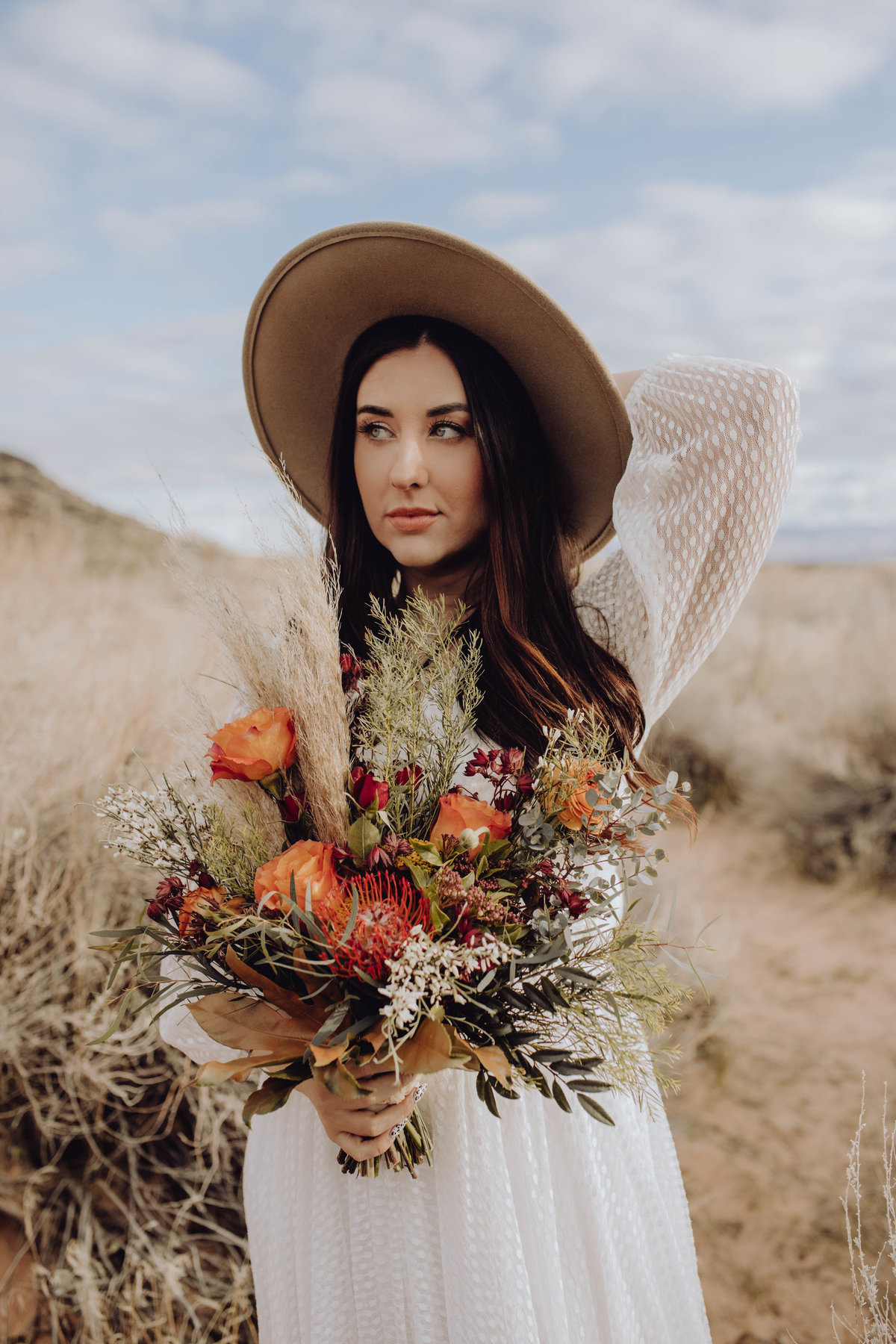 Bride with bouquet and holding hat behind her head outside of Snow Canyon