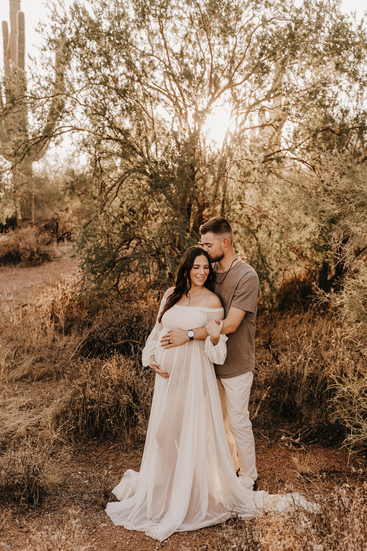mom in white chiffon gown posing with husband in desert for phoenix maternity session