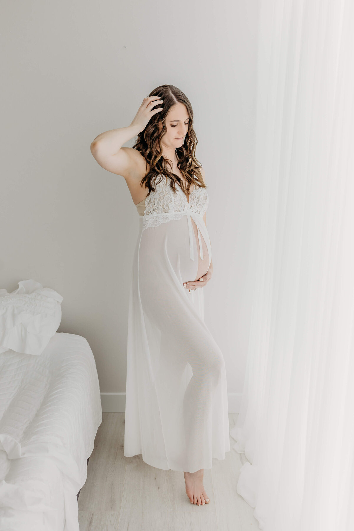 Full portrait of expecting mom in white maternity robe standing by window