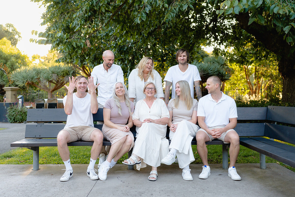 Extended family photography in Geelong capturing three generations sharing a joyful moment on a park bench, dressed in coordinated neutral tones.