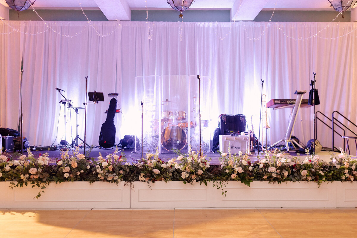November wedding at Graylyn Estate, designed and planned by Charming Carolina — reception dance floor and stage in the Atlantis Room with white draping, ceiling twinkle lights, and planter boxes filled with florals lining the front of the stage.