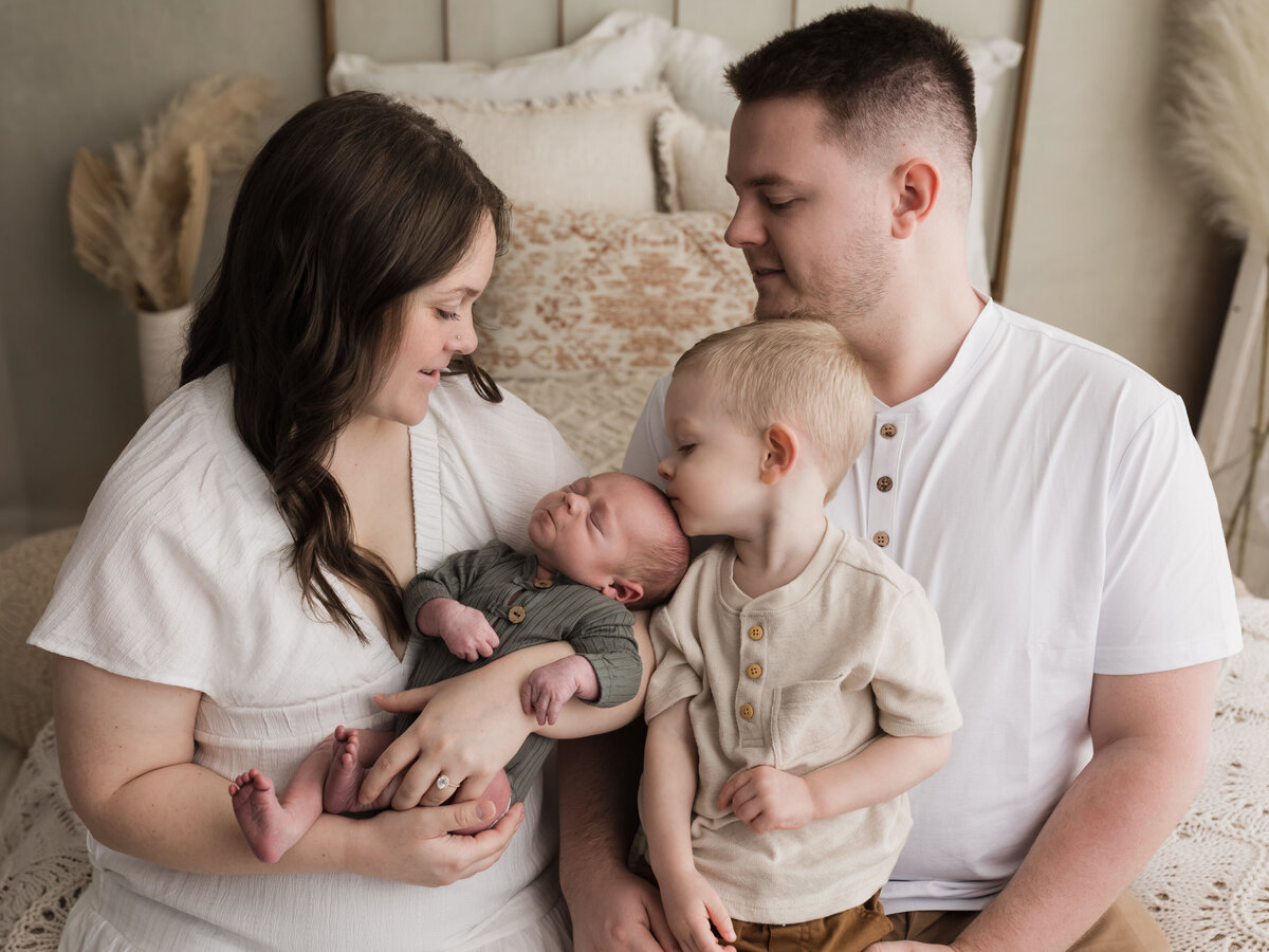 parents sitting on bed holding two year old son and newborn baby boy for studio portraits cleveland newborn photographer
