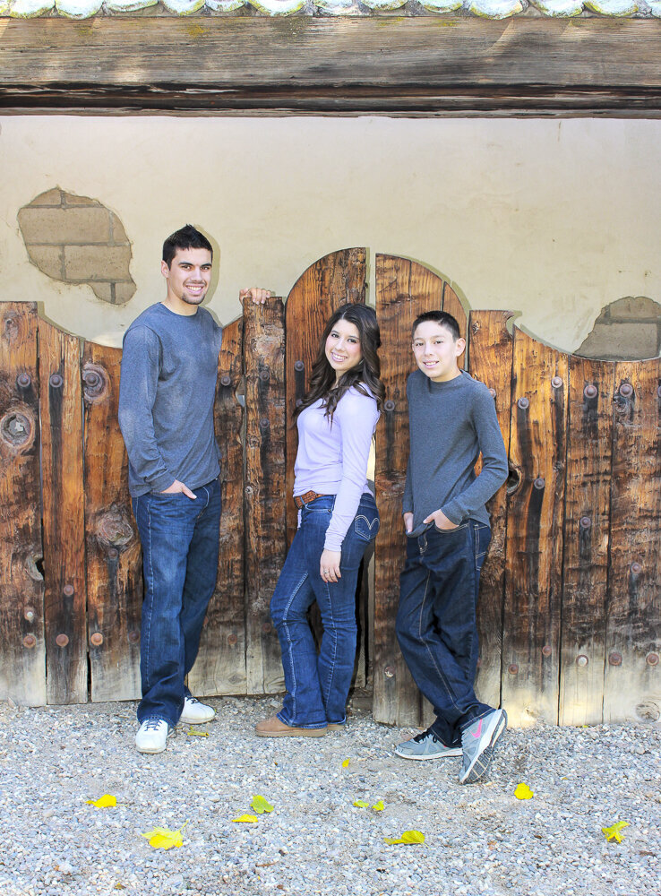 3 teenage siblings leaning on large fence with golden light