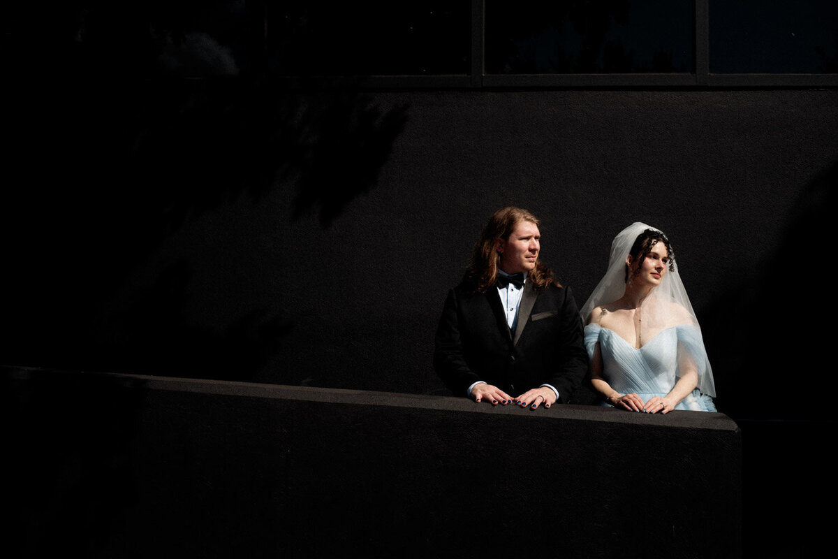 Black wall and lit by sun, couple stands stoic at elopement