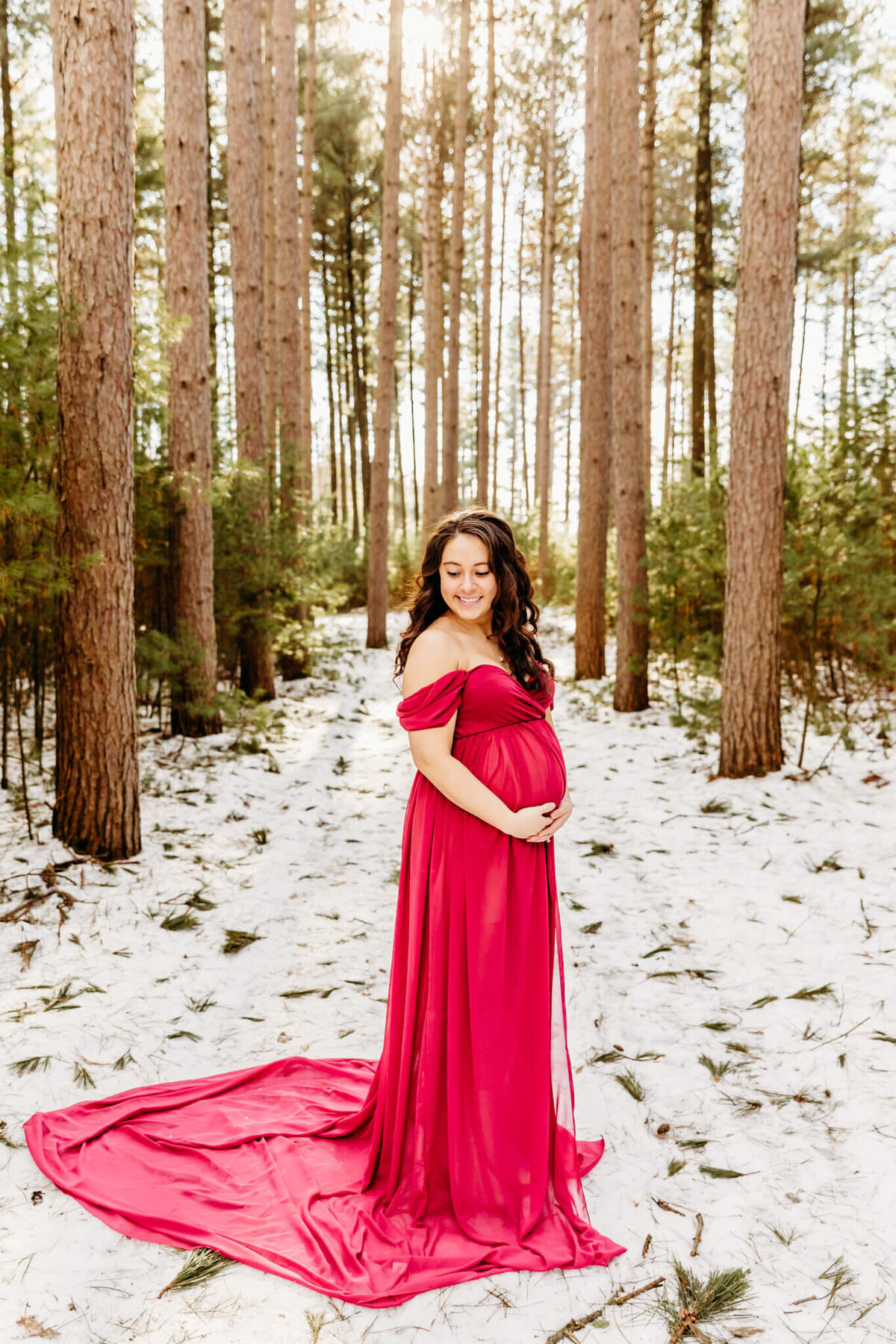 beautiful pregnant mother in a gorgeous pink gown holding her bump in a snowy forest  by Ashley Kalbus