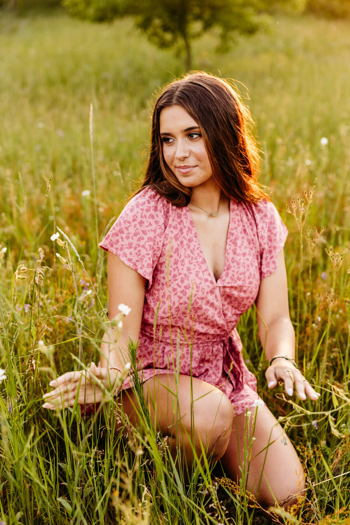stunning senior girl playing with the grass and flowers in a field as she looks out