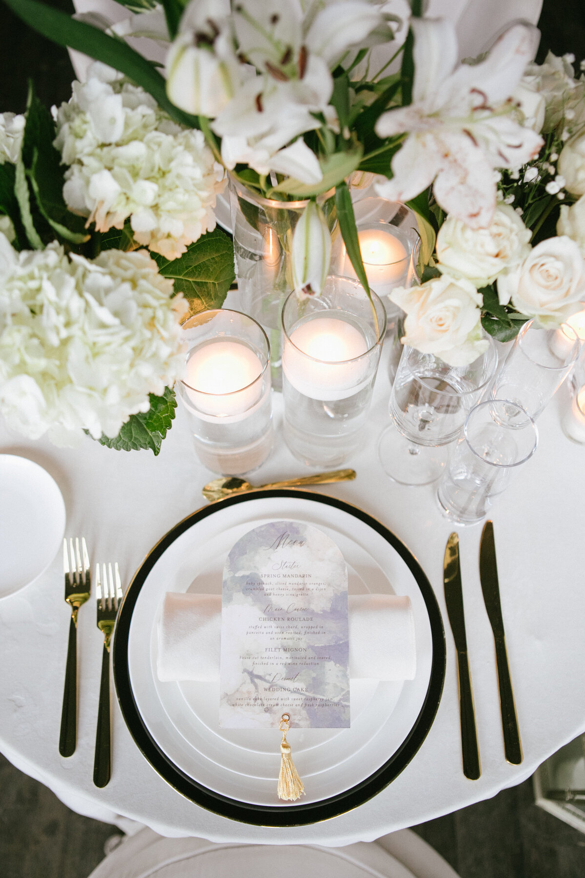 romantic wedding table setting featuring arched wedding menus, lush white floral and greenery centerpieces and candles.