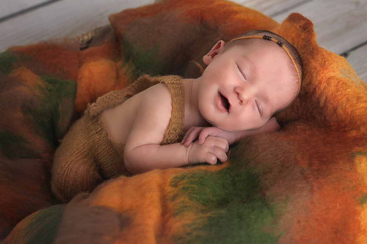Baby girl smiling while sleeping on her forest theme wool blanket during home photo session by Yuliia Terziian Photography in Calgary,Alberta