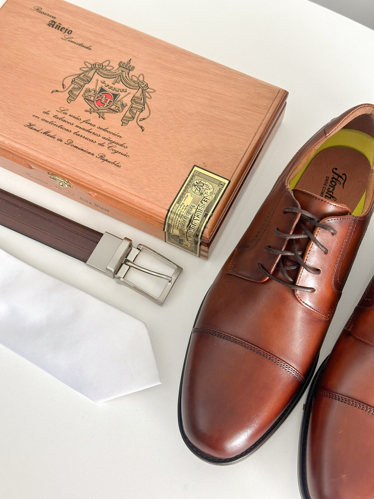 Groom shoes, belt, tie, and cigar box on a white mat at Lake San Marcos in San Diego, California.
