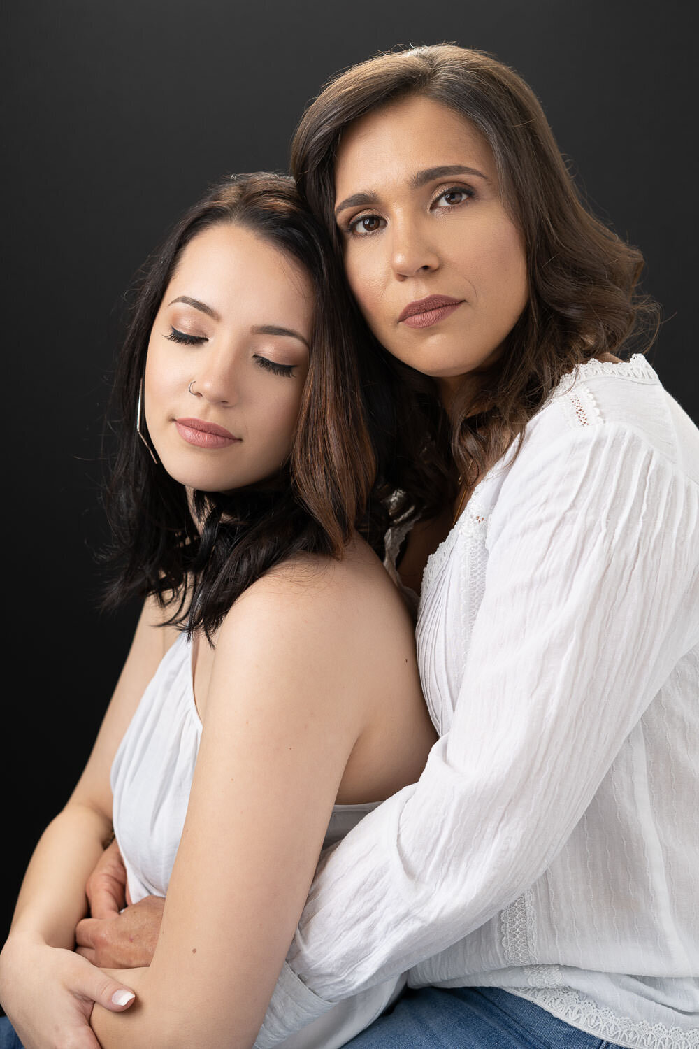 Studio portrait of a mother lovingly embracing her teen daughter, who sits peacefully with her eyes closed.
