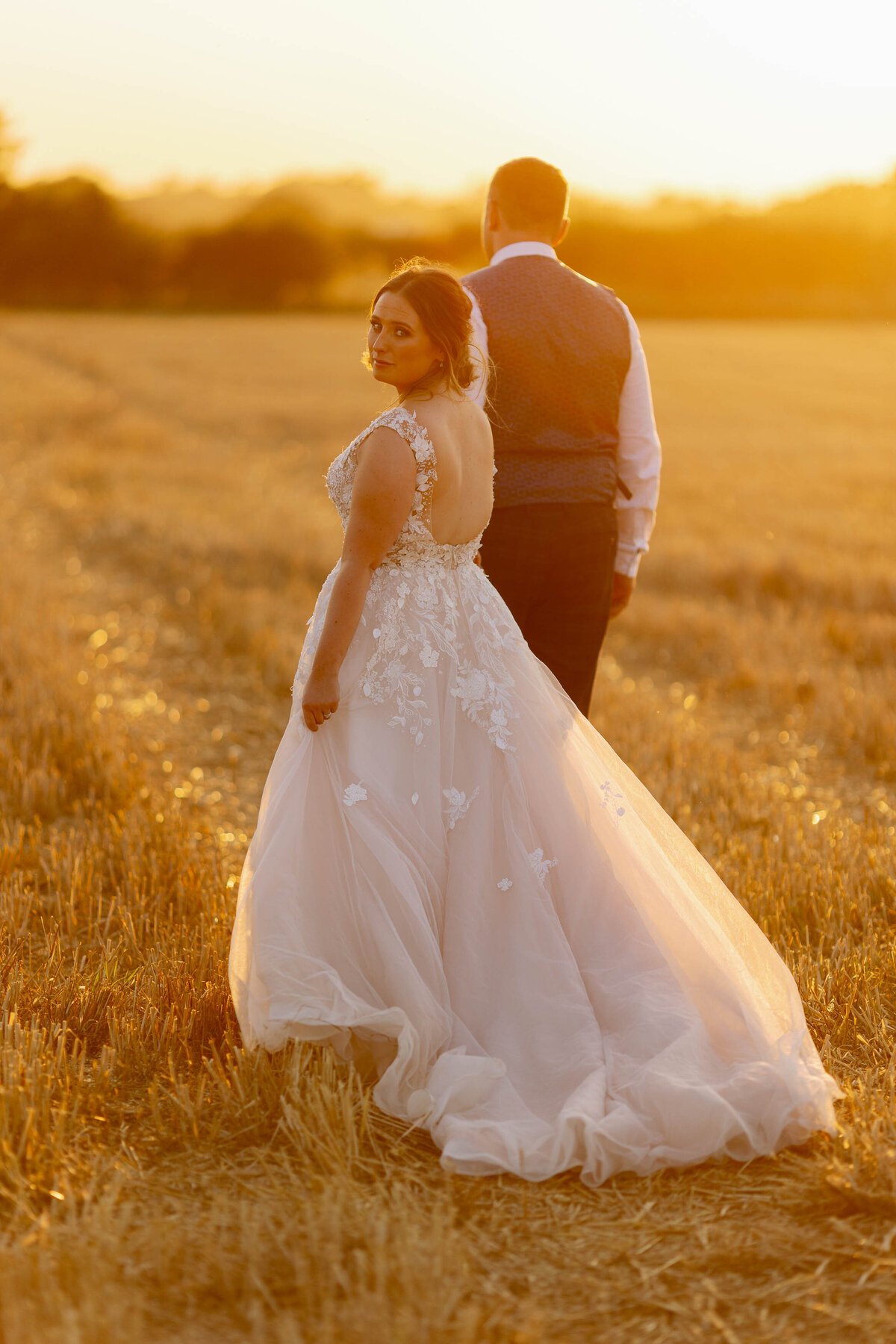 Bride looking back at camera as she walks in a corn field during golden hour