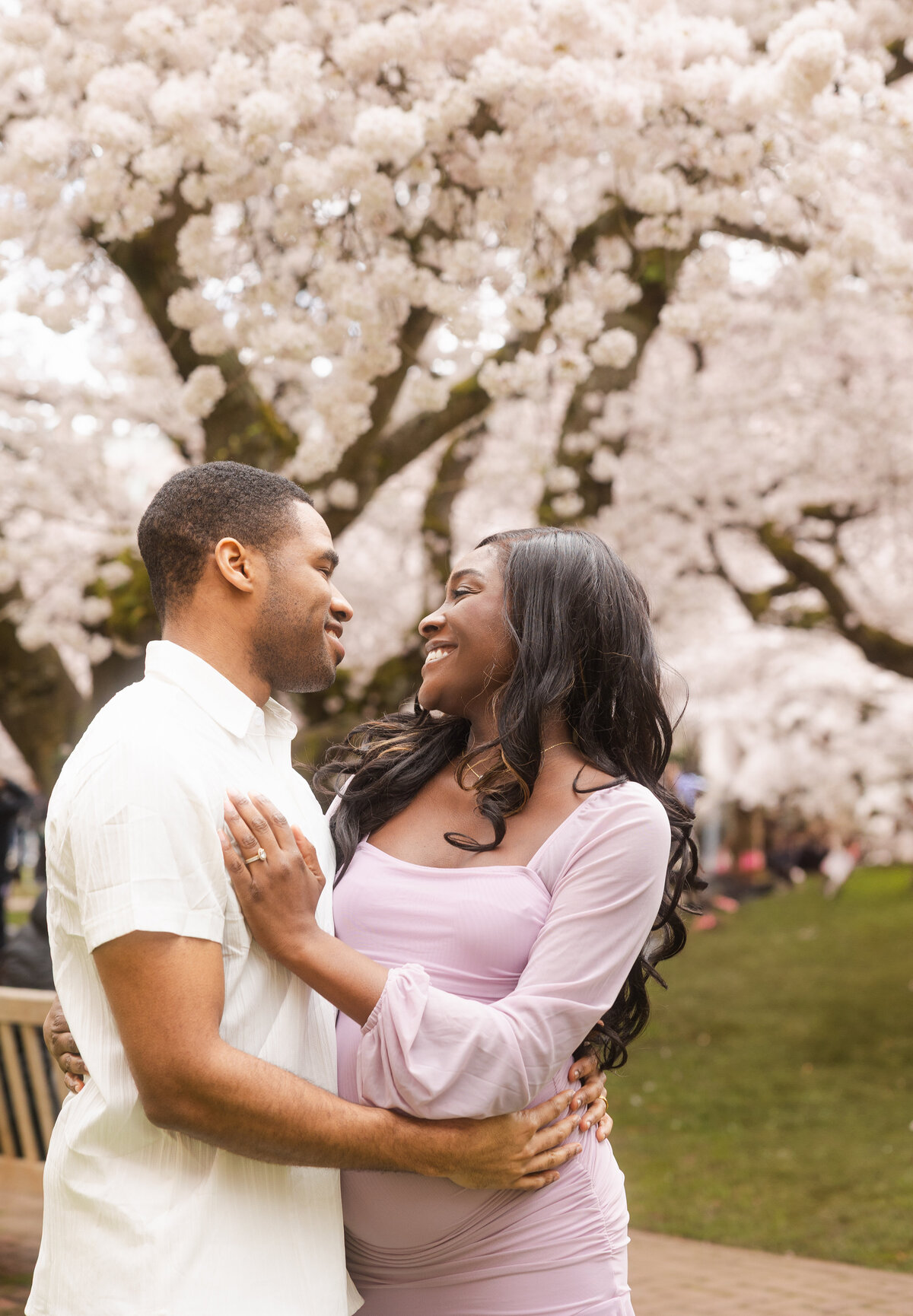 A romantic moment as the couple looks into each other's eyes, framed by the stunning cherry blossom trees at the University of Washington campus, surrounded by the beauty of nature and their love.