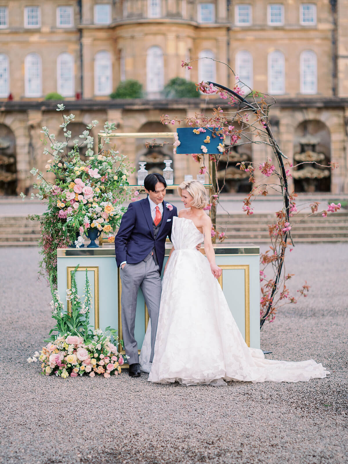 bride and groom standing at blenheim palace in front of a green vintage drinks reception bar decorated with pink and peach flowers and cherry blossoms