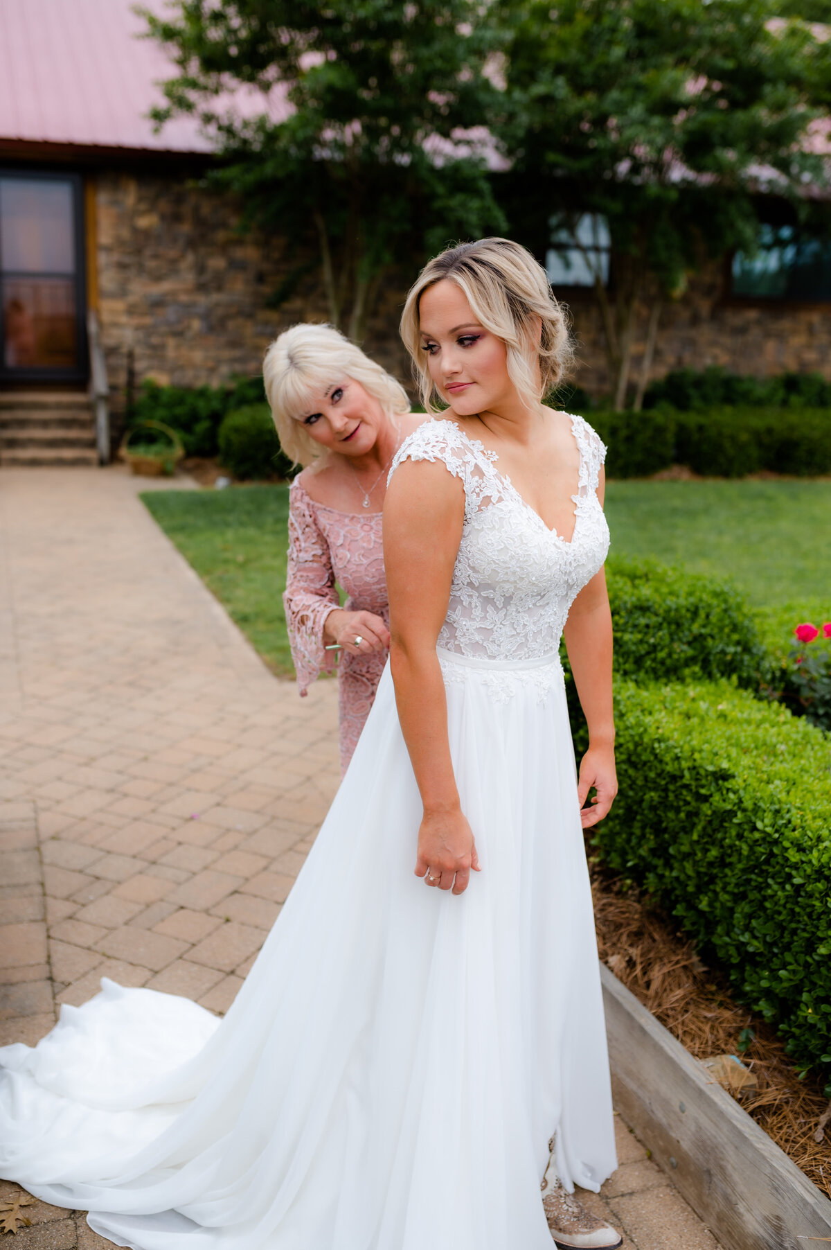 Little Rock wedding photographer captures mother of the bride zipping up the brides wedding dress as they standing together in and outdoor garden in little rock ar