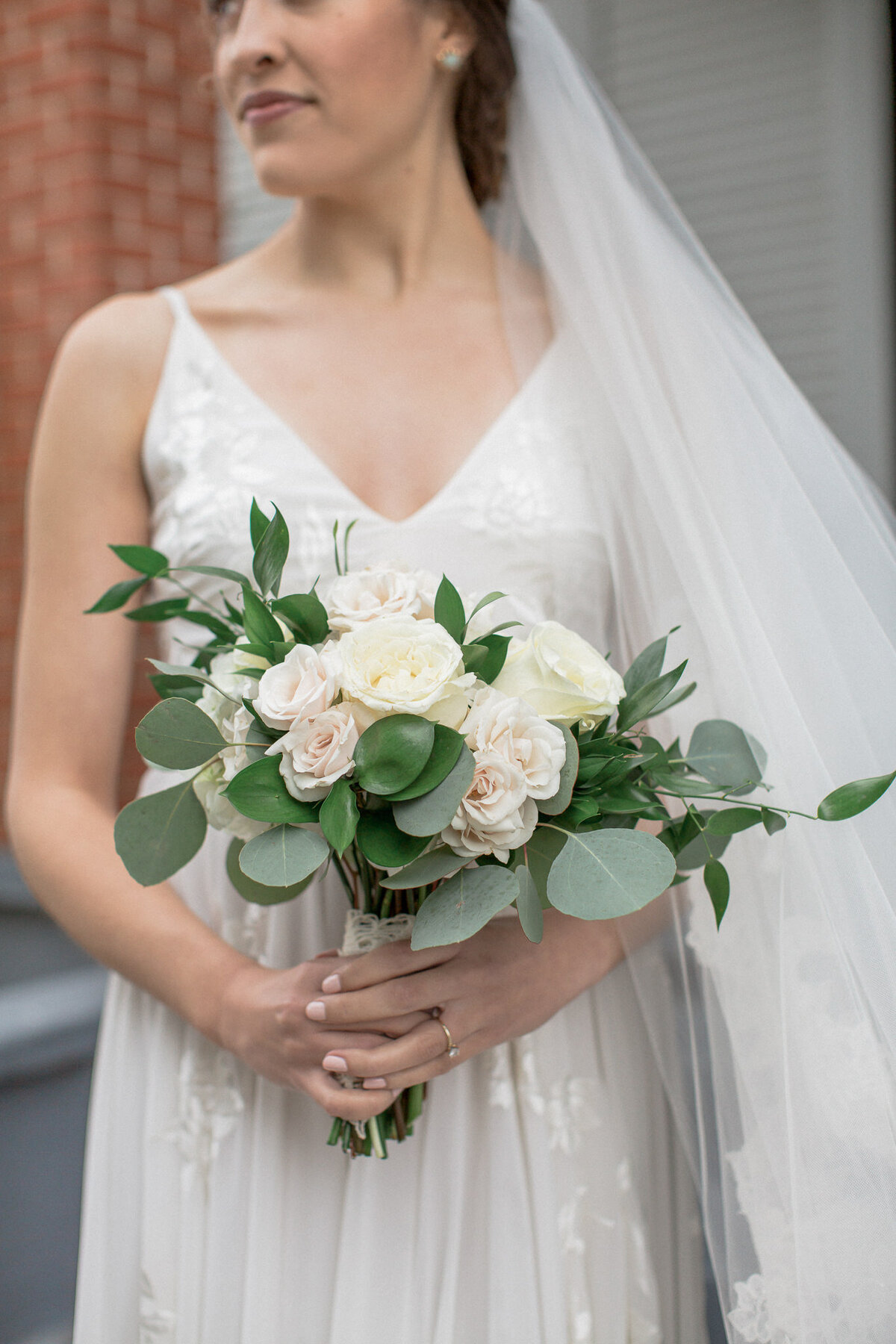 A close up photo of the bridal bouquet composed of white roses and eucalyptus, held by the bride