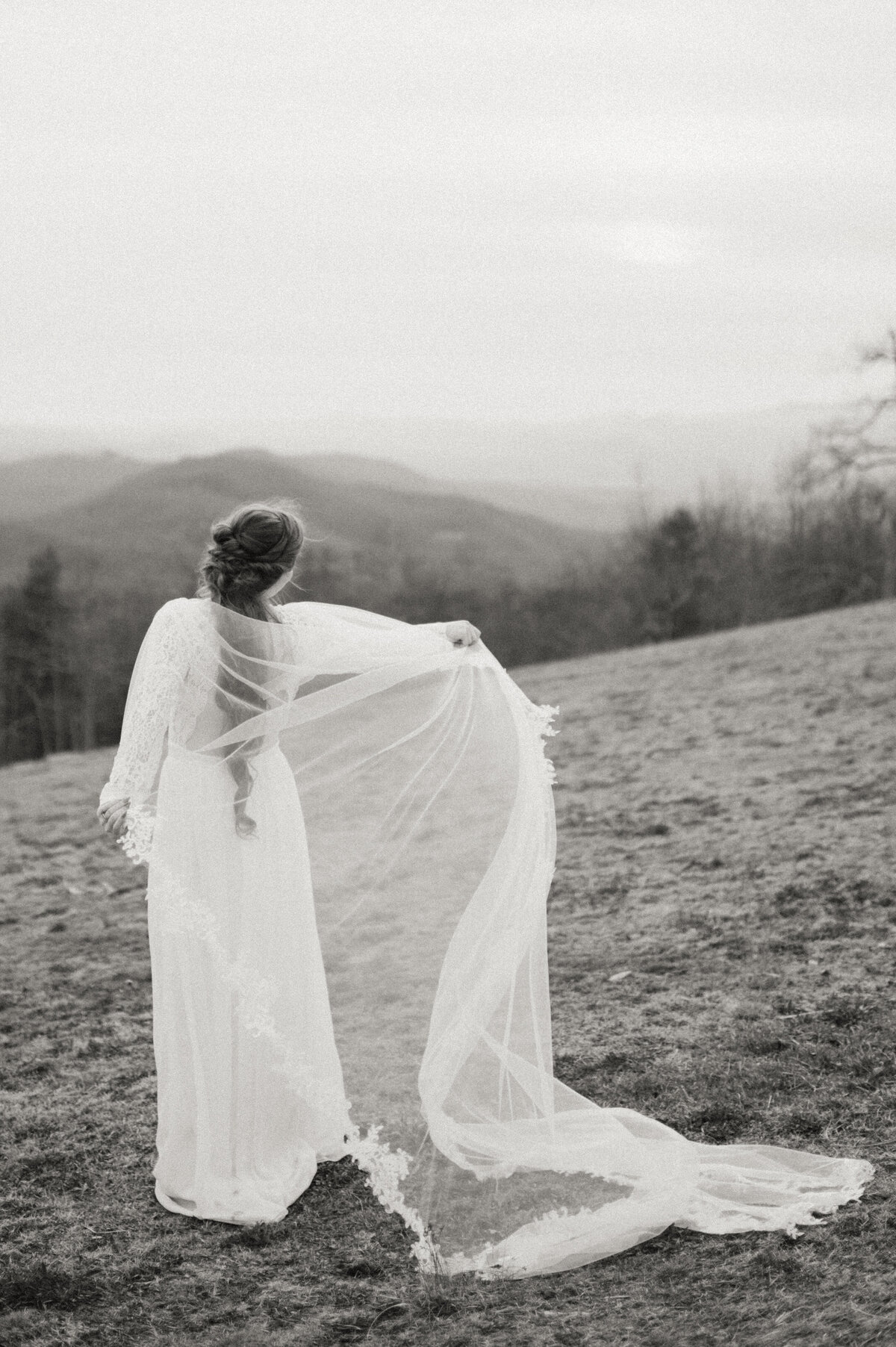 bride plays with dress cape with mountains in the background