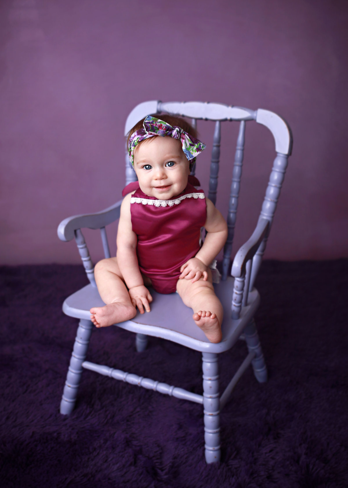 baby girl posed on purple chair against purple backdrop