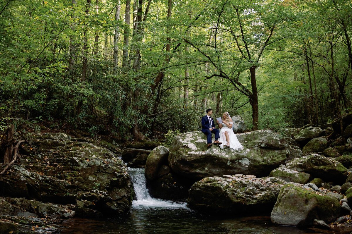 waterfall wedding pictures with bride adn groom sitting on the top of a waterfall reading notes to each other for their Smoky Mountain elopement