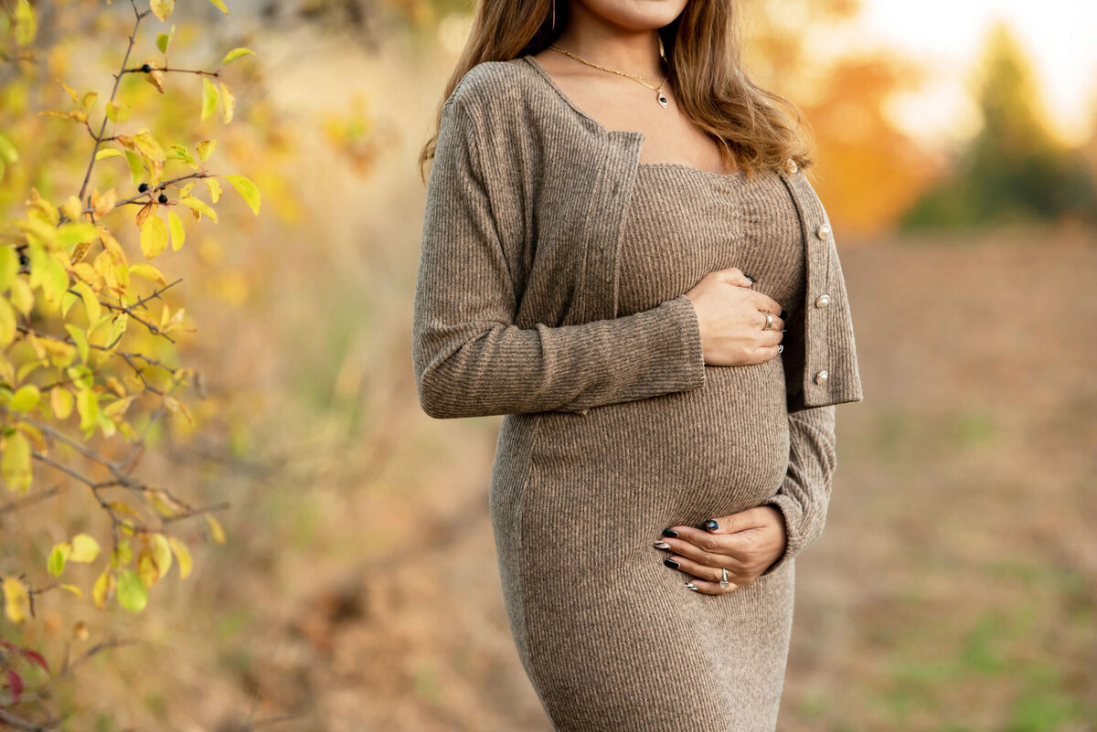 up-close photo of a pregnant woman holding her belly for her Fall maternity photos in Burlington