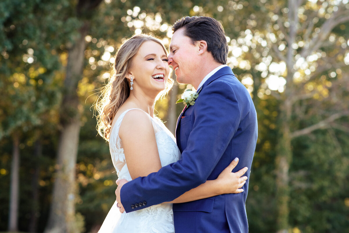 Bride-laughing-as-groom-smiles-and-whispers-in-her-ear-their-arms-around-each-other-on-the-golf-course-of-Pine-Island-Country-Club-in-Charlotte