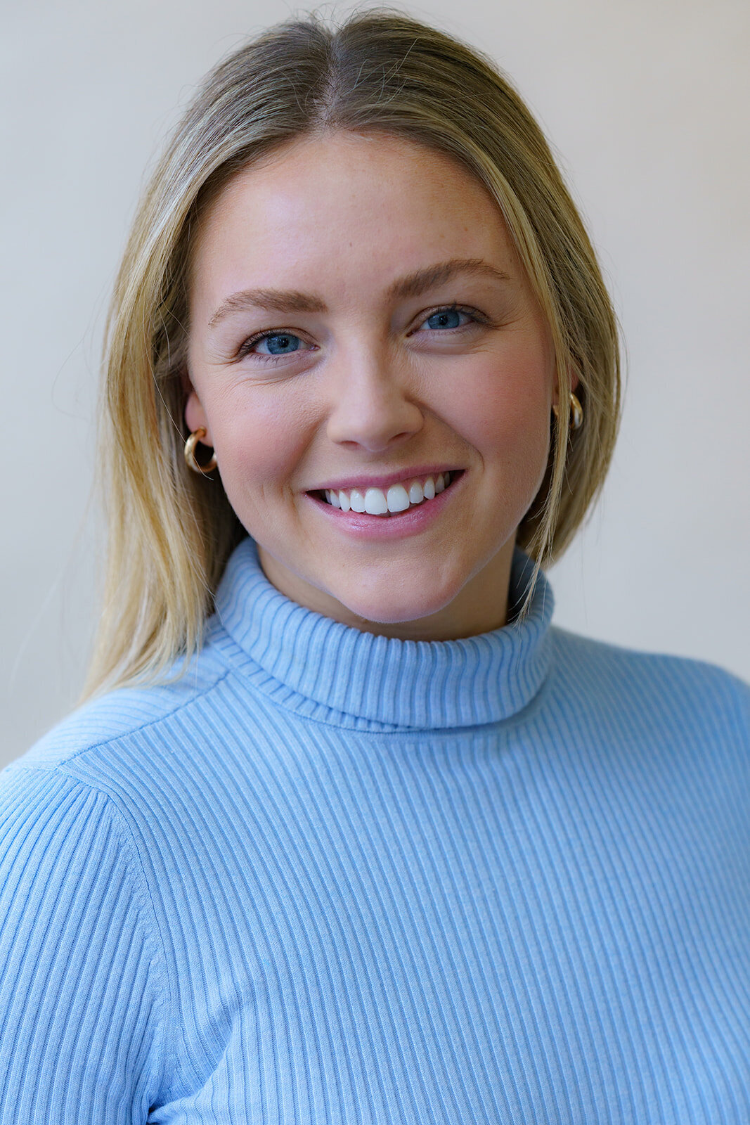 Young woman in a turtleneck sweater, long hair, and a welcoming smile posing for a headshot photo