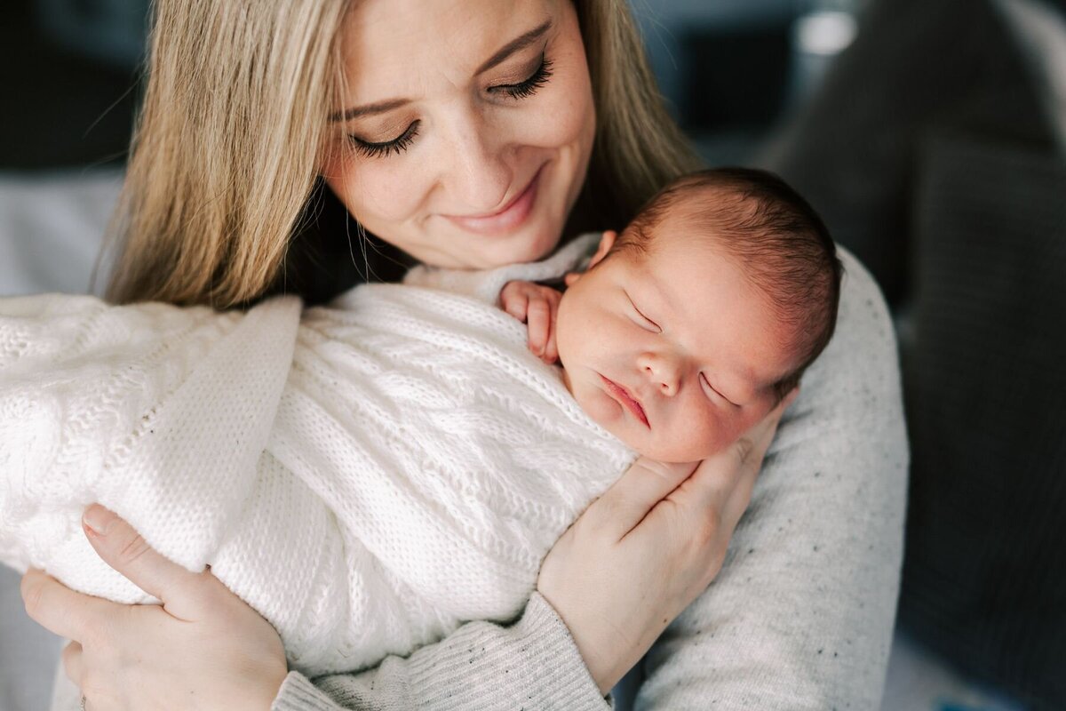 Mom smiles and baby as she holds him for his portraits during his newborn photography session.