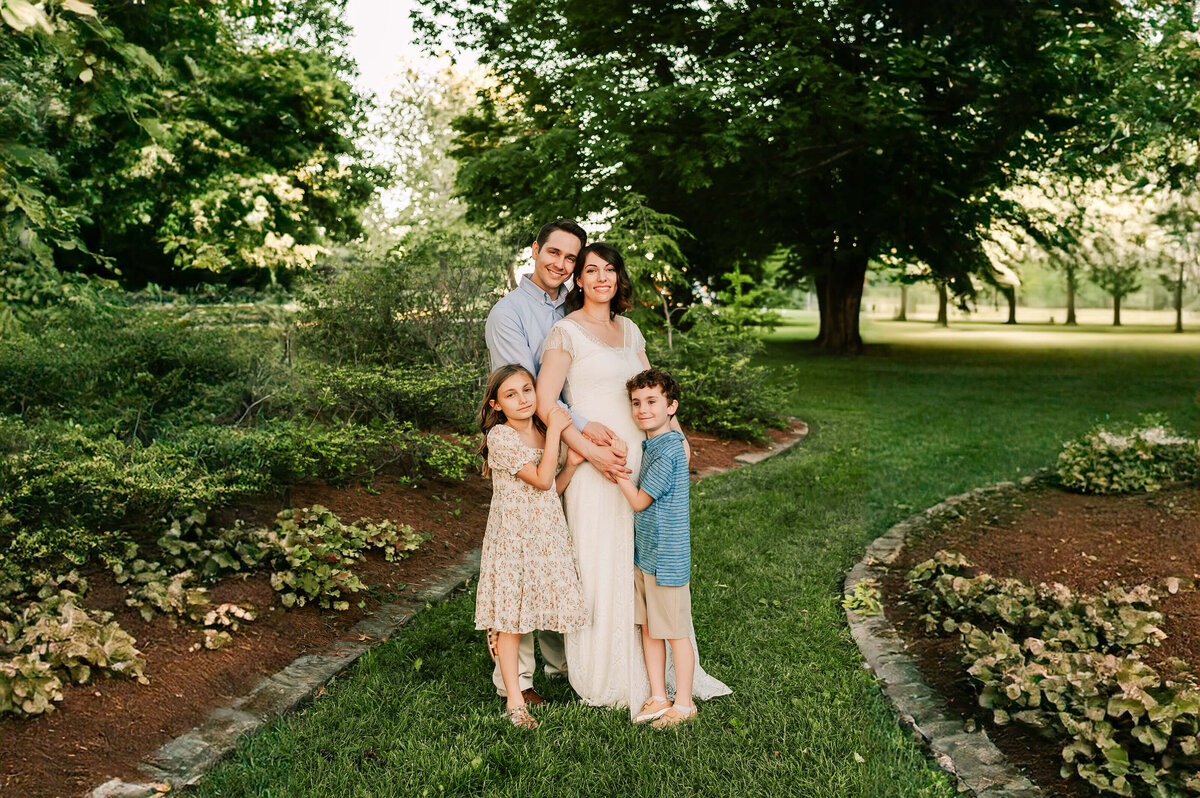 Springfield Mo newborn photographer Jessica Kennedy of The XO Photography captures pregnant mom being hugged by husband and older kids at Nathanial Greene Park in Springfield MO