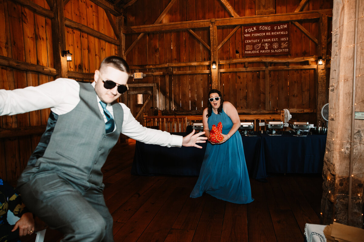 A groomsman and bridesmaid dance and play on the dance floor in a rustic barn venue